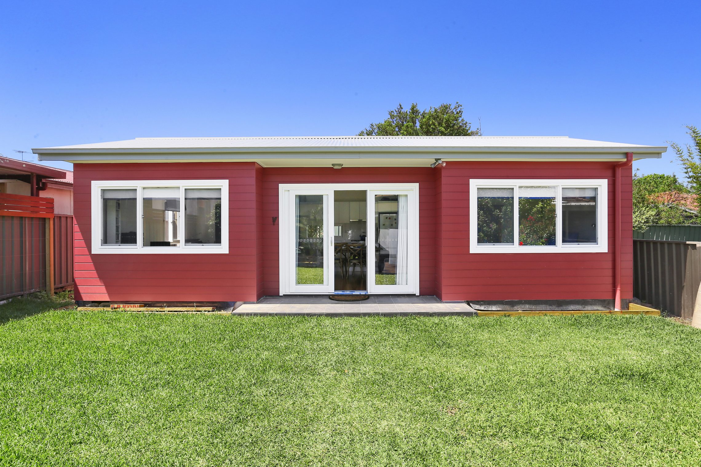 Barn red granny flat exterior with 3 panelled windows on either side of door entry