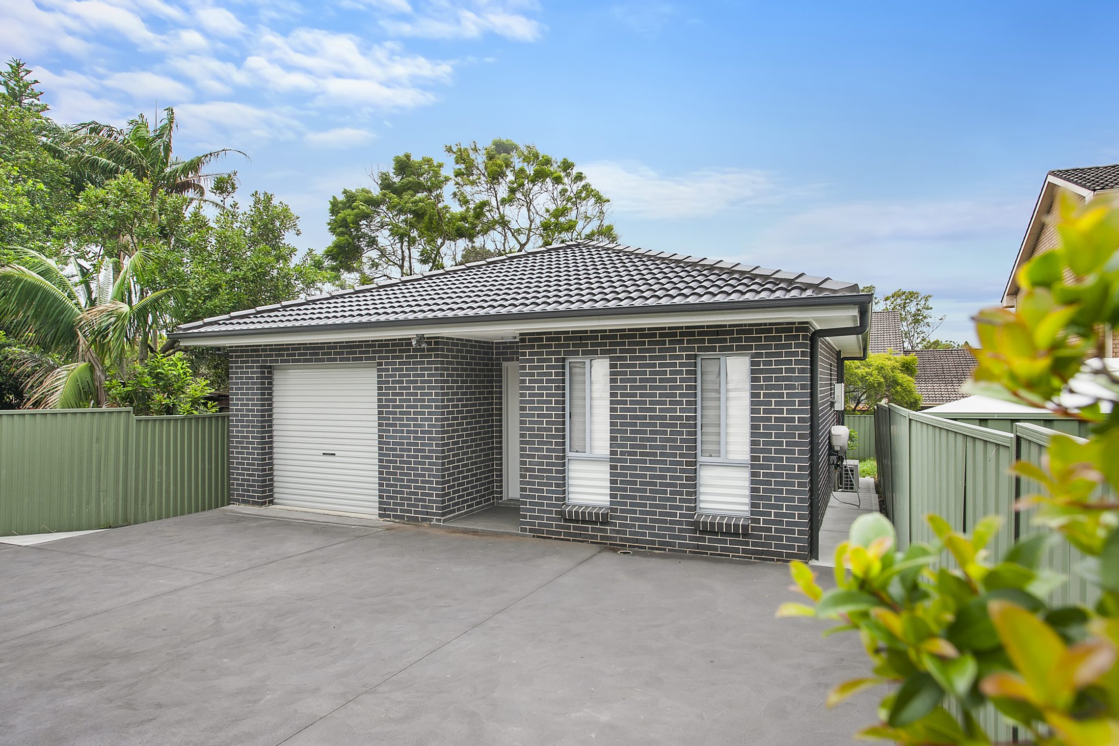 Small gray brick granny flat with single car garage and driveway