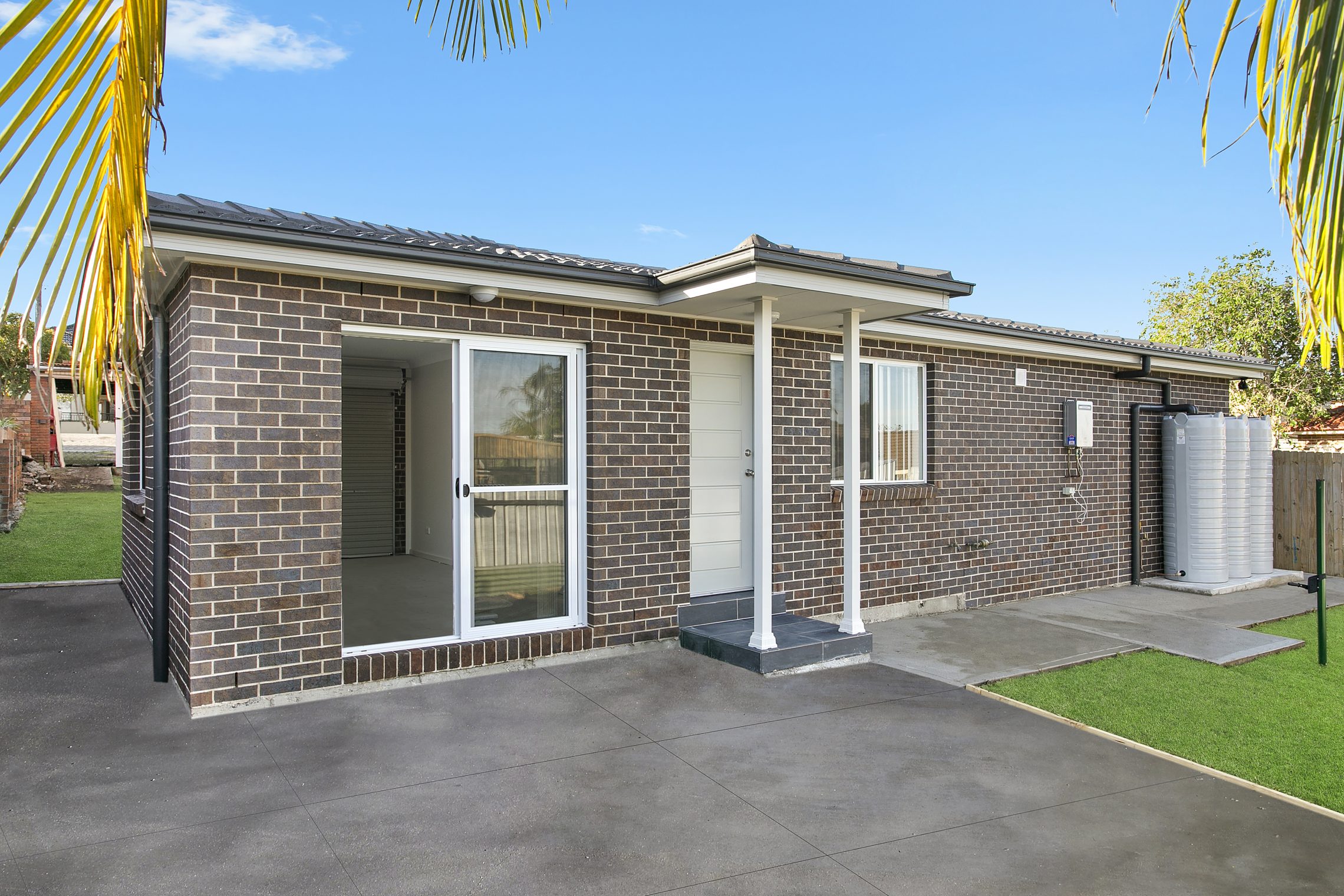 Dark brick granny flat with driveway and both single door and sliding glass doors entry points