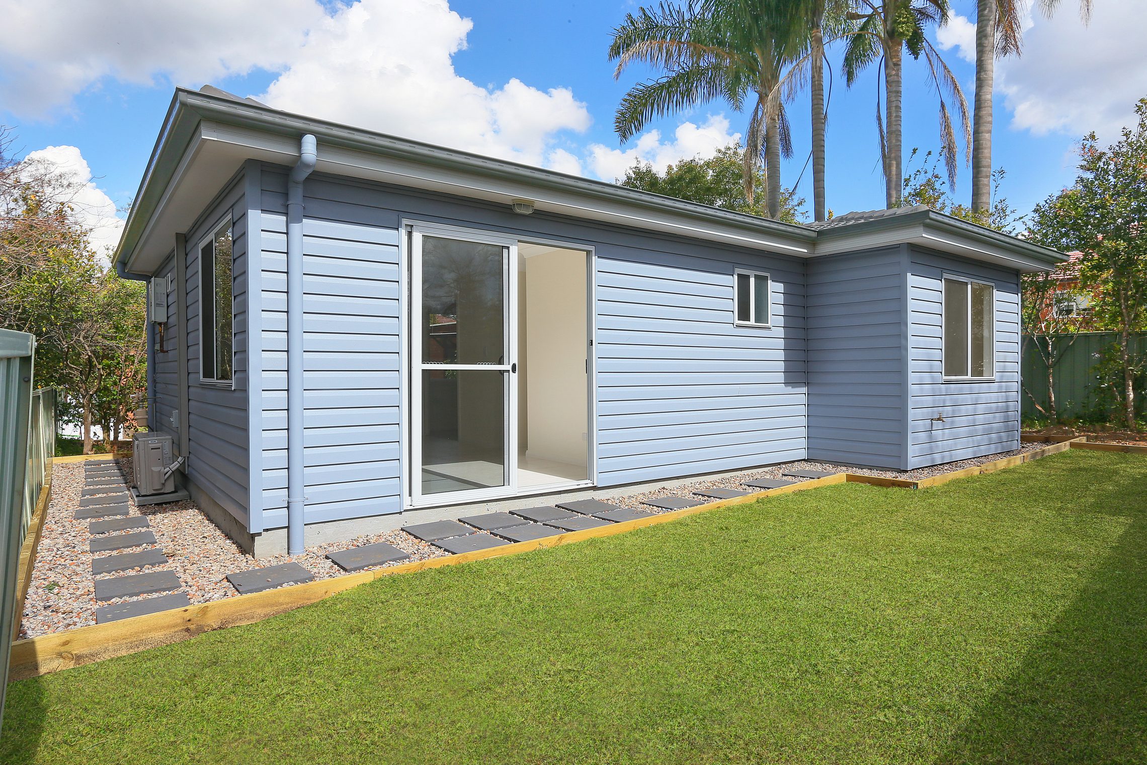 Back exterior of blue granny flat with concrete walkway squares around building