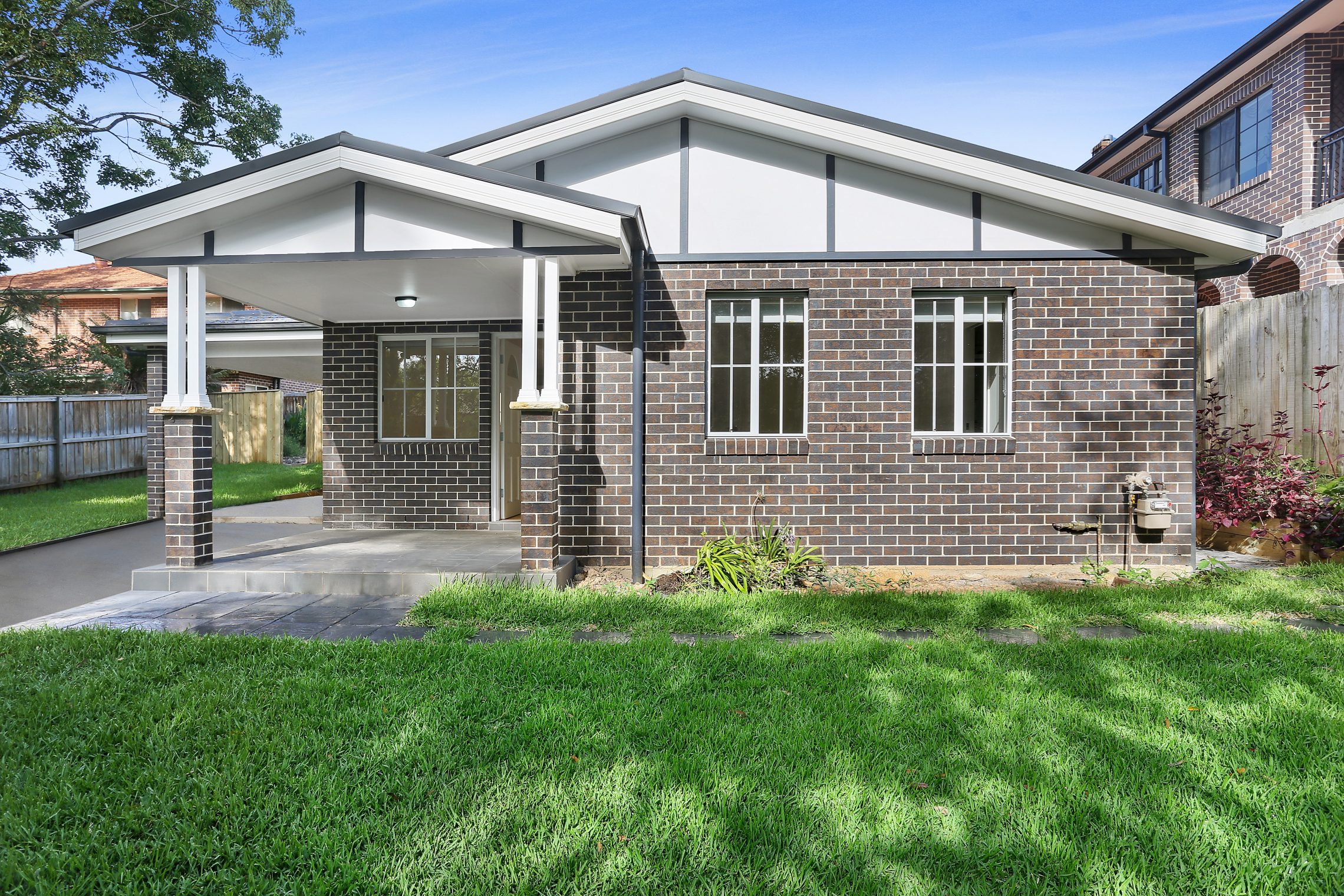 Dark brick granny flat with covered entry connecting to driveway