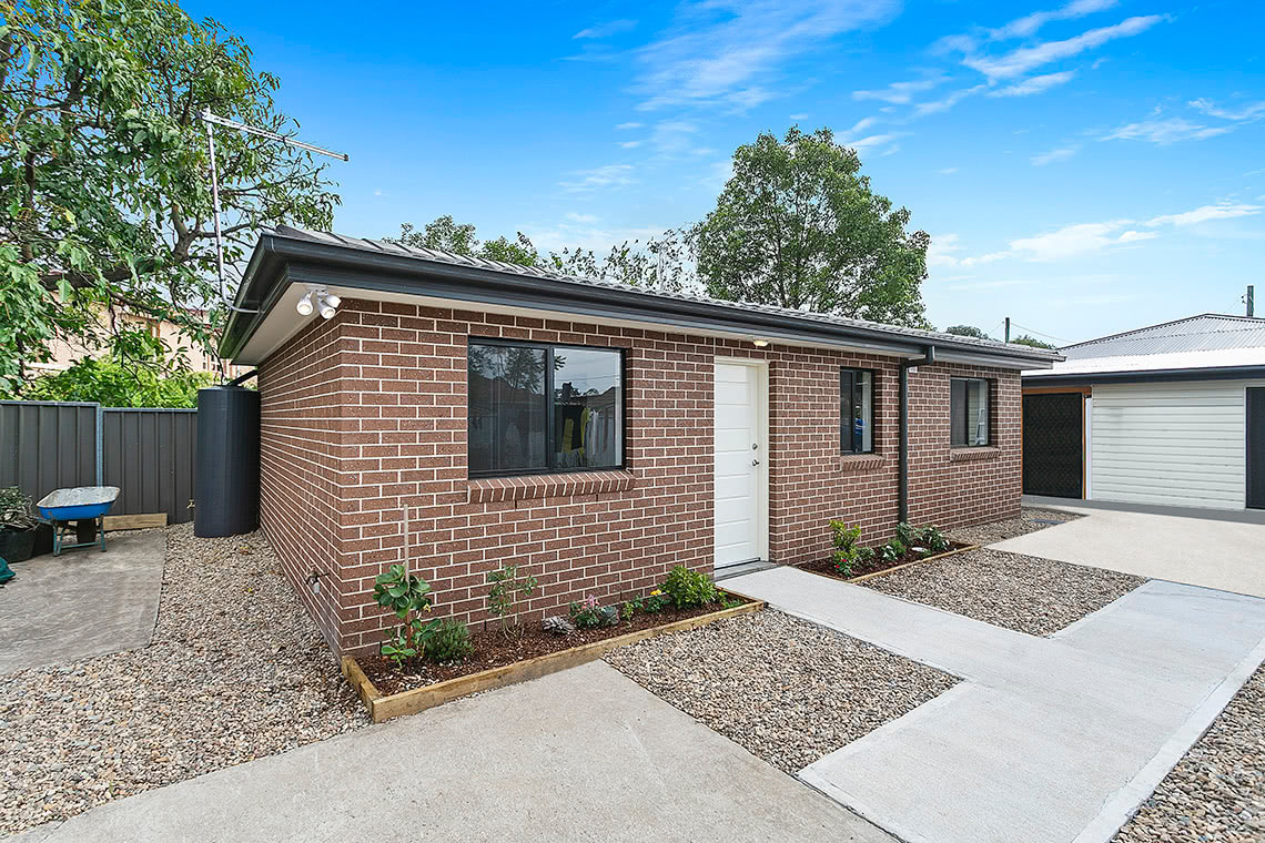 Small brick granny flat with outdoor walkway leading to driveway